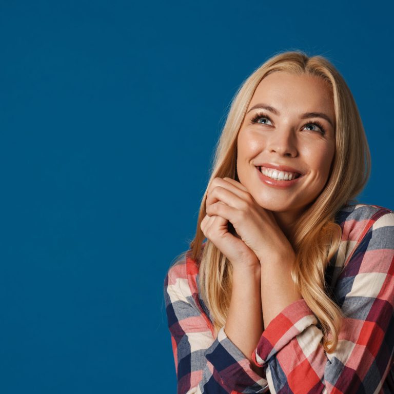 Blonde young happy woman smiling and looking upward isolated over blue background