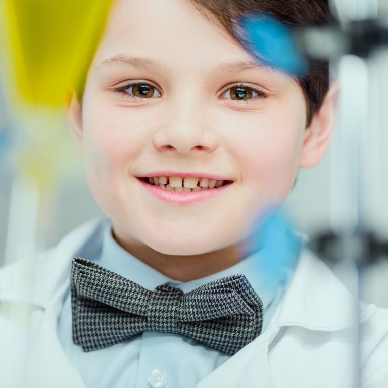 Close-up portrait of cute smiling schoolboy in lab coat looking at camera, science school concept
