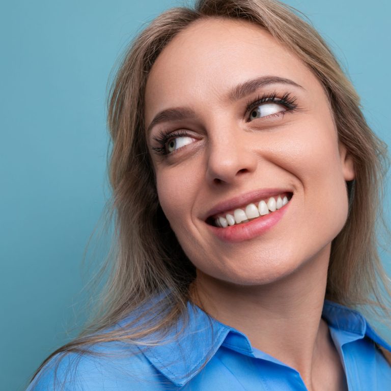 photo of shy cute casual young woman with smiling eyes on bright blue background.