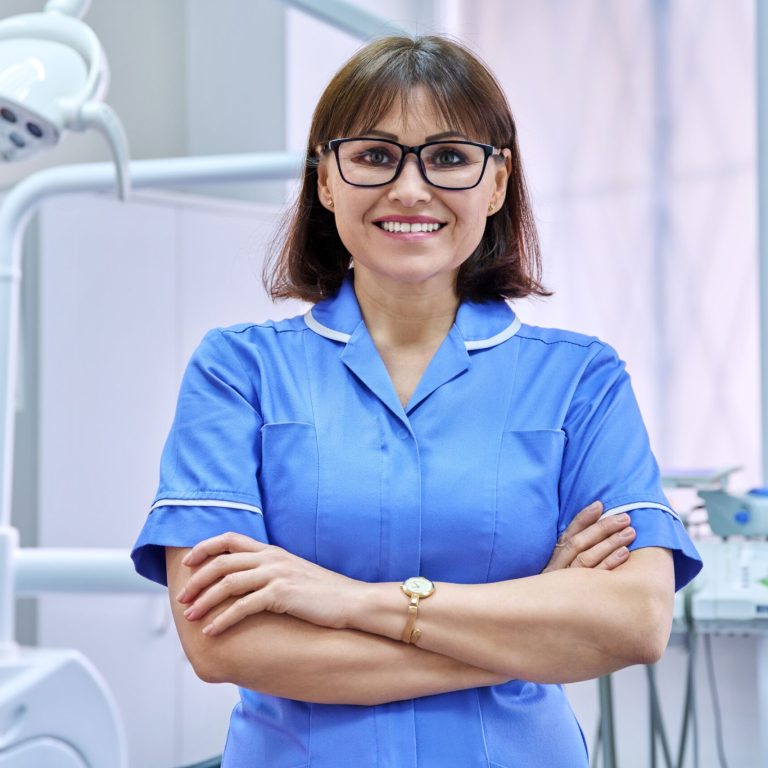 Portrait of smiling nurse looking at camera in dentistry. Confident female with folded hands, dental clinic equipment background. Dentistry, medicine, health care, profession, stomatology concept