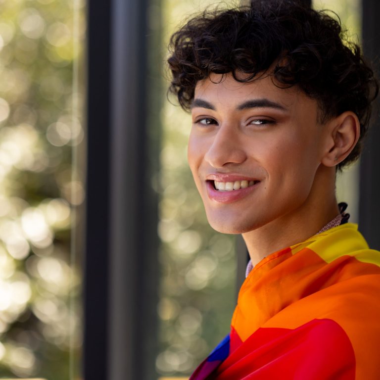 Smiling transgender woman wrapped in rainbow flag, celebrating LGBTQ+ pride at home, copy space. celebration, diversity, inclusion, joy, happiness, equality