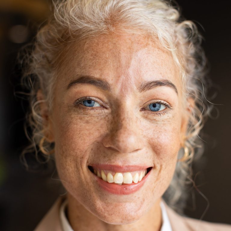 Smiling woman with curly hair and freckles, close-up portrait in office setting. smile, professional, workplace, business, confident