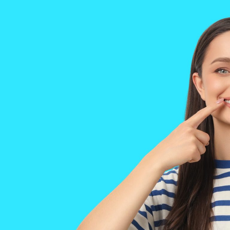 Woman points at her smile on a bright blue backdrop